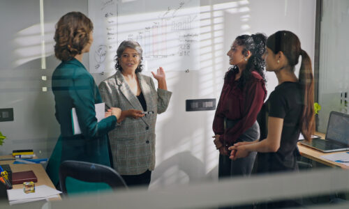 Woman speaks to group while presenting statistics on whiteboard