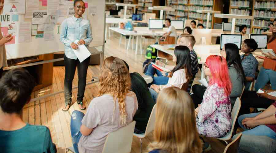 A child speaks to a room of seated people in a library