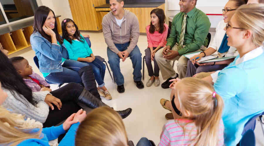 A photo of parents and children sitting in a circle, laughing, at school.