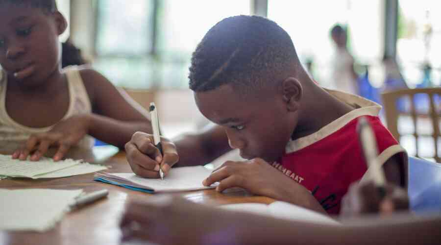 A young Black boy focuses on his assignment at school, pencil in hand.