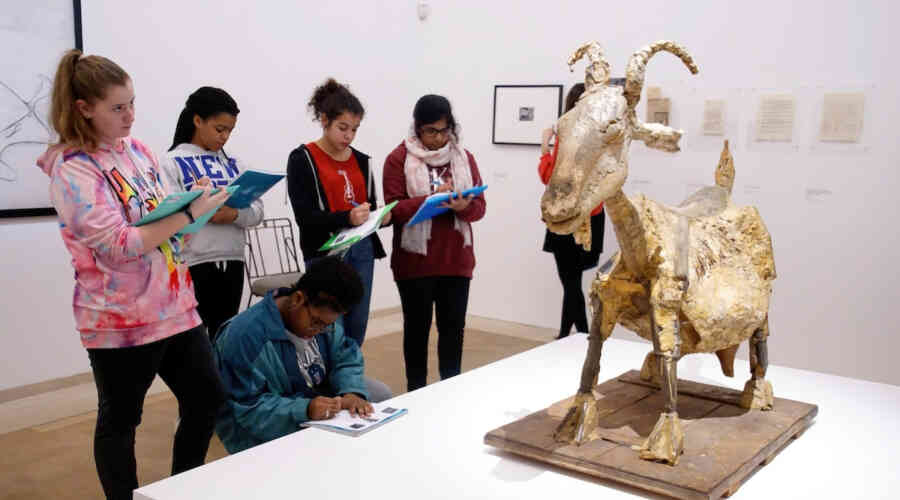 Young adults examining a sculpture of a goat and taking notes.