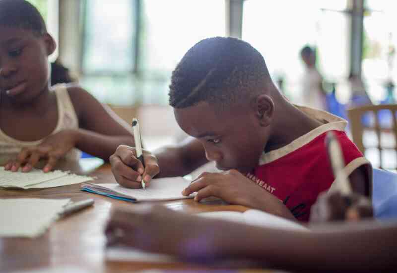 A young Black boy focuses on his assignment at school, pencil in hand.