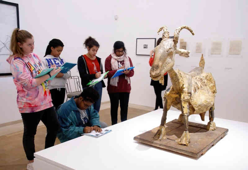 Young adults examining a sculpture of a goat and taking notes.