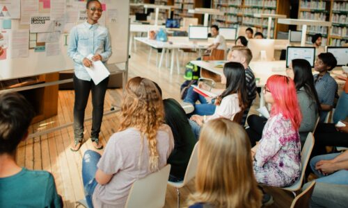 A child speaks to a room of seated people in a library