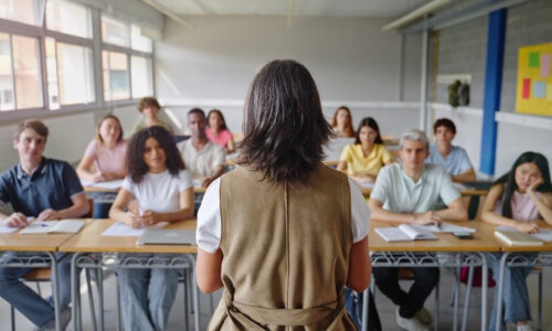 A classroom full of students face a teacher, with the camera facing the back of the teachers head