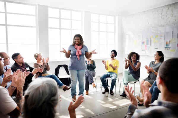 A woman stands in the center of a circle of seated people while they clap